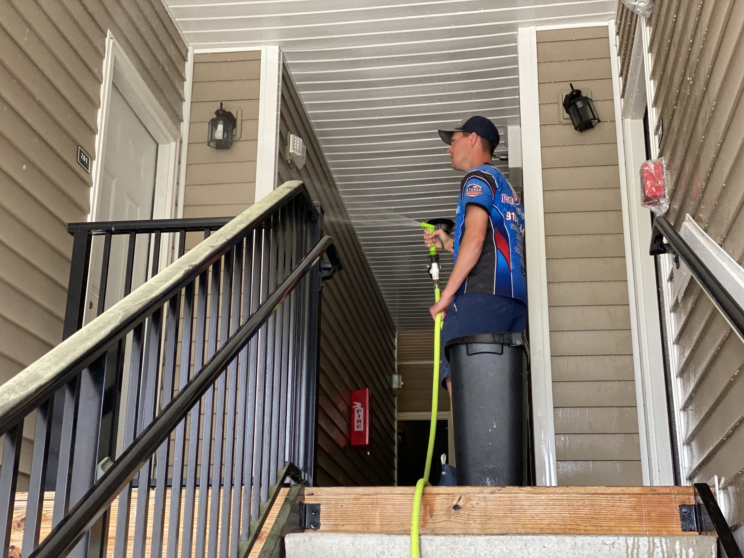 Patriot Softwash technician soft washing an apartment breezeway in Raleigh, NC, with sensitive equipment covered for protection