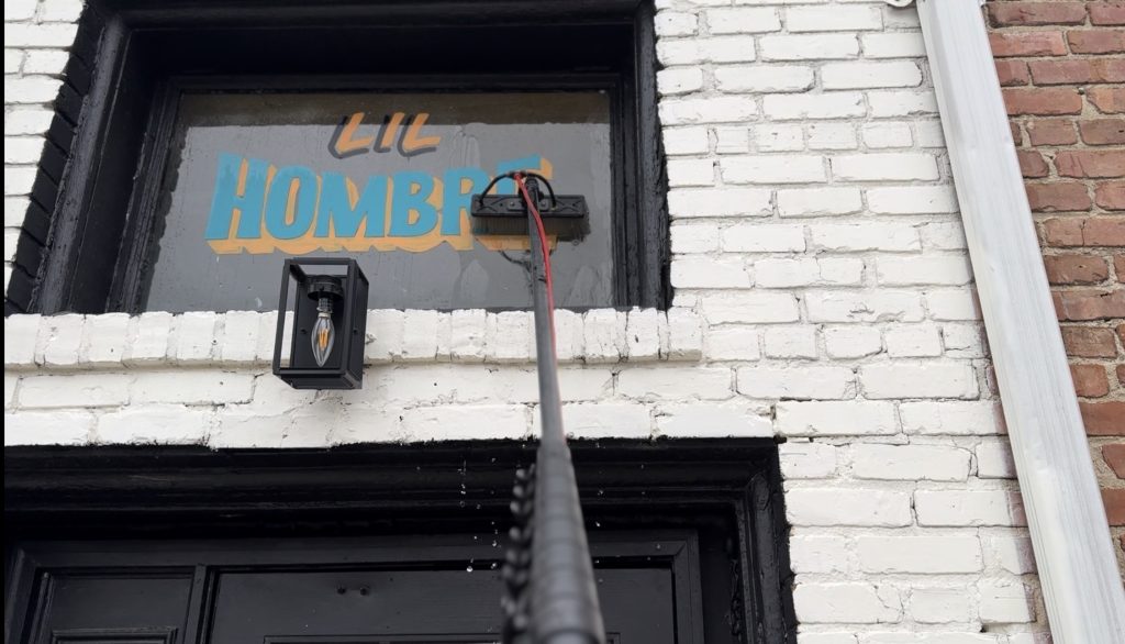 Patriot Softwash cleaning upper storefront windows with a water-fed pole at Little Hombre in Clayton, NC